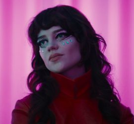 Une femme maquillée sous les yeux de perles bleus posent devant un rideau rose dans Her Private Hell de Nicolas Winding Refn