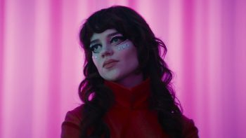 Une femme maquillée sous les yeux de perles bleus posent devant un rideau rose dans Her Private Hell de Nicolas Winding Refn