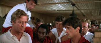 escape-to-victory-caine-stallone-john-huston Michael Caine en train de réfléchir sur la gauche du plan ; il est entouré par les joueurs dont l'un est Sylvester Stallone ; plan du film ESCAPE TO VICTORY de John Huston.
