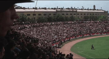 Vu des tribunes d'un stade plein de supporters et d'un bout de pelouse.