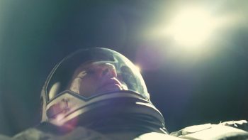Un astronaute, joué par Matthew McConaughey, est filmé en contre-plongée ; on aperçoit son visage dans un casque, tandis qu'un astre semble rayonner dans les ténèbres au-dessus de sa tête ; l'astronaute a l'air d'avoir les yeux fermés et de relever légèrement le visage ; plan du film INTERSTELLAR de Christopher Nolan. 