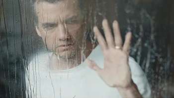 Un homme en tee shirt blanc (Wagner Moura) pose sa main sur une vitre ou coule de l'eau. Il semble inquiet et soucieux