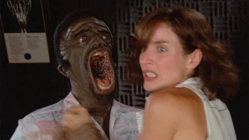Une créature à la peau noire et à la bouche béante agresse une femme visiblement effrayée ; la créature humanoïde est sur la gauche, effrayante, tandis que la femme est sur la droite, en détournant le visage ; plan du film THE STUFF, réédité par Rimini.