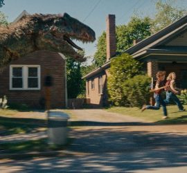 Un dinosaure géant poursuit deux personnes dans une rue résidentielle américaine.