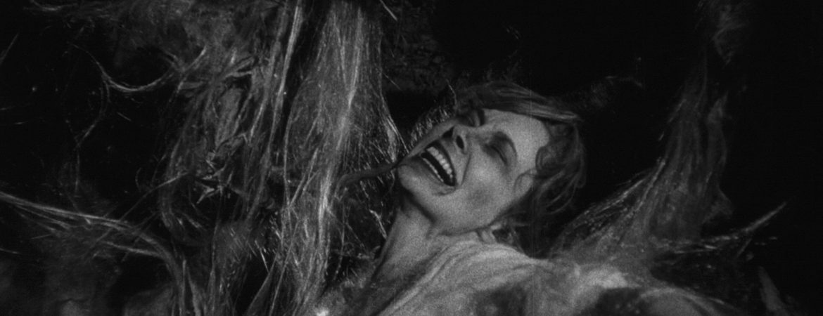 Personnage féminin coincée dans ce qui ressemble à de longs fils épais pour faire un cocon ; plan issu du film la bête de la caverne hantée de Monte Hellman.