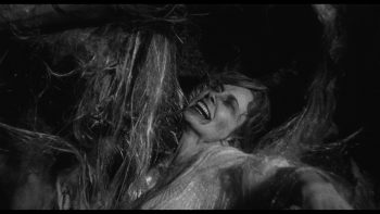 Personnage féminin coincée dans ce qui ressemble à de longs fils épais pour faire un cocon ; plan issu du film la bête de la caverne hantée de Monte Hellman.