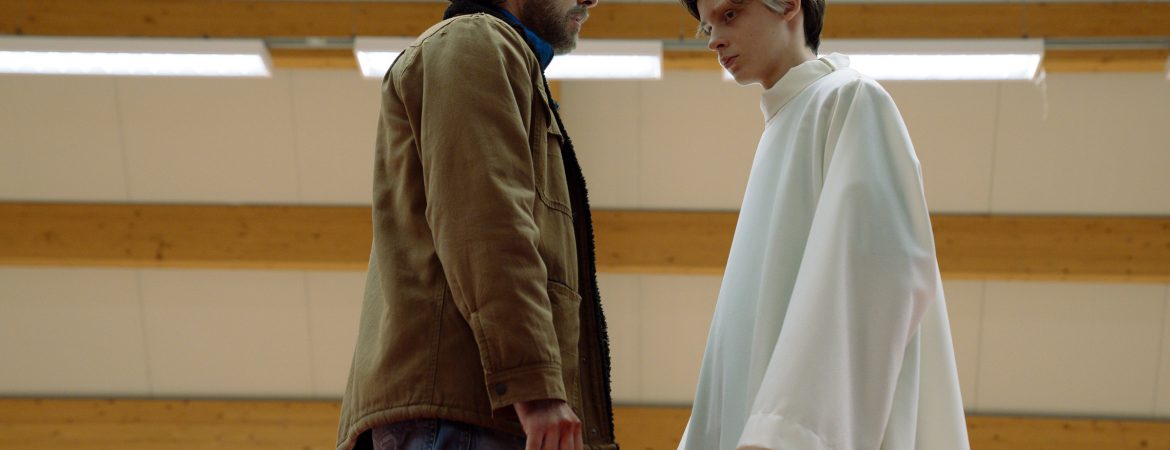 Un face à face entre un homme et l'enfant saint du film , dans un gymnase ; plan issu du film The Holy boy de Paolo Strippoli.