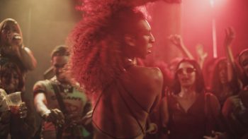 A Margem do Rio / The Riverbank : une femme danse au milieu d’une foule sous des lumières rouges.