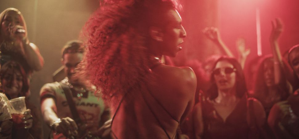 A Margem do Rio / The Riverbank : une femme danse au milieu d’une foule sous des lumières rouges.