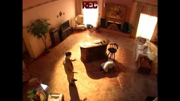 Moniteur d'une des caméras de l'émission "To catch a predator", caméra placée haut cadrant un salon en plan d'ensemble ; Chris Hansen, joué par Robert Pattinson est debout face à un des hommes piégés ; plan du film PRIMETIME de Lance Oppenheim.