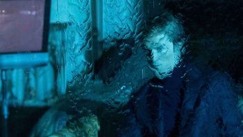 Robert Pattinson vu derrière une vitre troublée par une intense pluie ; plan issu du film PRIMETIME de Lance Oppenheim.