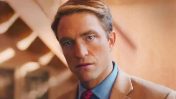 Plan rapproché-épaule sur Robert Pattinson dans le film Primetime, regardant dans l'objectif avec un regard à la fois flottant et dirigé ; plan du film PRIMETIME de Lance Oppenheim.