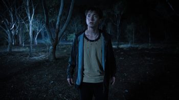 Un adolescent seul la nuit dans une forêt, le regard attiré vers quelque chose que l'on ne voit pas ; plan issu du film Leviticus de Adrian Chiarella.
