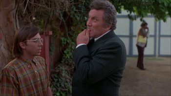 Deux hommes face à face sur le côté gauche de l'image semblent discuter, même s'ils ne se regardent pas ; l'un est un jeune homme à lunettes et chemise à carreaux ; l'autre est plus âgé et semble réfléchir ; son menton dans la main tandis qu'un autre homme est en arrière plan ; plan issu du film le silence qui tue de Denny Harris.