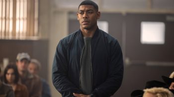 Aaron Pierre, interprète de John Stewart ; regarde droit devant lui dans ce qui semble être un gymnase ou se réunissent les gens ; plan issu de la série Lanterns.
