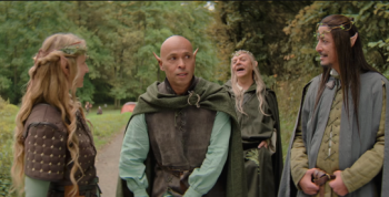 Éric Judor en costume médiéval entouré de personnages aux oreilles pointues dans une scène du film Le Roi du Game.