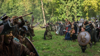 Des orcs armés de haches affrontent un groupe de guerriers et d'elfes dans une clairière forestière du film Le Roi du Game d'Éric Judor.